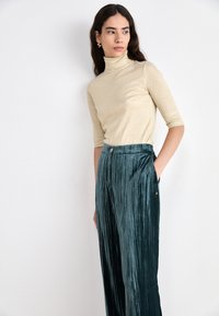 Haut en col roulé beige ajusté à manches courtes associé à un pantalon large plissé teal avec un léger brillant et des poches latérales.
