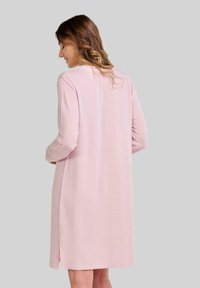 Vestido rosa de manga larga con corte recto, textura suave, aberturas laterales y escote redondo, que presenta costuras decorativas en la parte trasera.