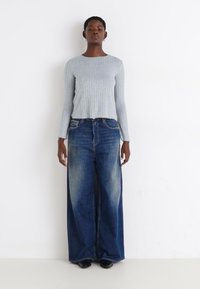 Lys grå ribbet langermet topp kombinert med vide mørkeblå denimjeans, med en falmet vask og lett slitasje ved lommeåpningene.