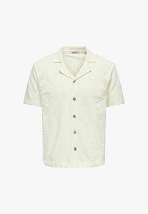 Chemise crème à manches courtes avec col ouvert, cinq boutons marron et motifs floraux délicats en maille sur les côtés avant.