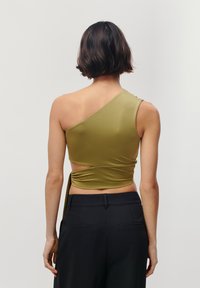 Asymmetrical olive green top with one shoulder, featuring a fitted design and knotted detail, paired with black trousers.