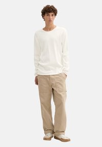 Weißes langärmliges Rippenhemd, beige Cargo-Hosen mit Taschen und beige Sneaker. Einfaches Design mit lässiger Passform und neutralen Farben.