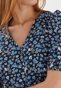 Svart blommig klänning med blåa och vita blommor, korta puffärmar och V-ringning med knappar, tillverkad av lättviktsmaterial.