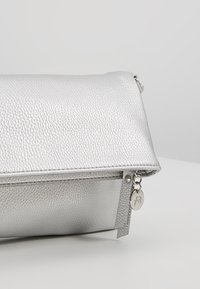Silver leather clutch bag with a textured surface, zipper closure, and a small metal tag accent. Rectangular shape, sleek design.