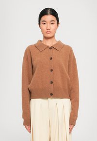 Brun, oversized kardigan med bred krage og seks brune knapper. Har et mykt, teksturert stoff og ribbede mansjetter og kant.