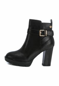 Bota de cuero negro hasta el tobillo con un tacón grueso, que presenta una correa decorativa y un hebilla dorada. Acabado texturizado y detalles de costura en relieve.