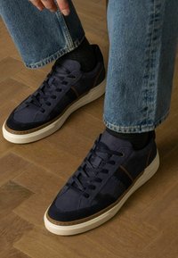 Marine sneakers met suede en leren panelen, witte zool en bruine accenten. Veters parallel, textiel met textuur en zichtbaar stikseldetail.