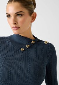 Granatowy prążkowany top dzianinowy z usztywnianym kołnierzem, ozdobiony złotymi guzikami w kształcie liści oraz teksturowanym wykończeniem.