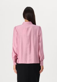 Blusa rosa de manga longa com gola, ombros plissados e pulsos abotoados. Textura suave, ajuste descontraído e design de cor sólida.