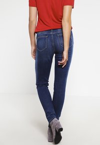 Jeans ajustados en denim azul oscuro con una textura suave, que presentan dos bolsillos traseros, costuras sutiles y un diseño ajustado.