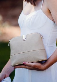 Světlobéžová kožená kabelka s texturovaným povrchem, stříbrnými kovovými prvky a zipovým uzávěrem. Navržena s hladkým spodním pruhem.