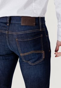 Jeans de mezclilla azul oscuro con costuras naranjas, que cuentan con cinco bolsillos, un parche de cuero en la parte trasera y un diseño de corte recto.