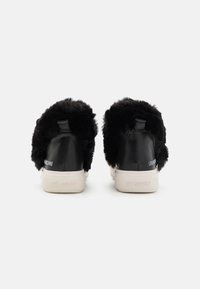 Svarta lädersneakers med fluffiga svarta pälsdetaljer. Har en beige gummisula och logotyp på hälen och sidan. Låg toppdesign.