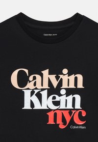 Camiseta negra con texto grande y multicolor: "Calvin Klein", "nyc" y "Calvin Klein Jeans". Tejido suave con diseño de cuello redondo.
