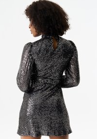 Black, sequin-covered dress featuring long puffed sleeves, high collar, and a small back keyhole detail. Smooth texture with shimmering accents.