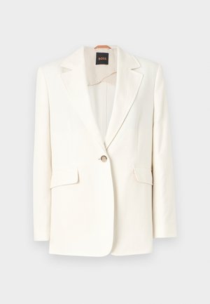 Blazer branco ajustado com lapela de pico, fecho de botão único e dois bolsos frontais. Tecido suave e linhas limpas. Etiqueta da marca visível no interior.