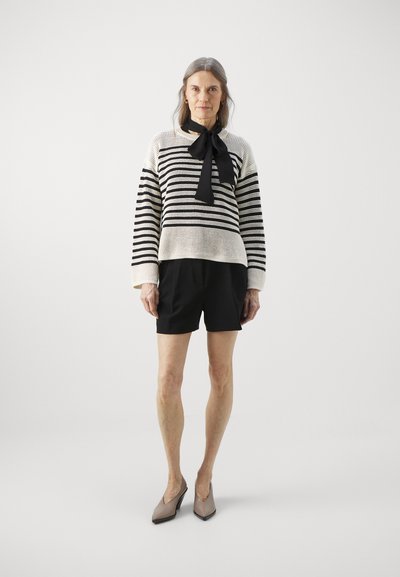 Pull en maille rayé noir et crème avec des manches larges et un nœud noir. Associé à un short noir et des escarpins beiges pointus.