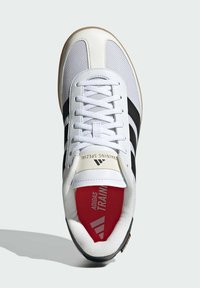 White sneaker with black stripes, textured mesh upper, rubber sole, padded collar, red insole, and branded tongue label.