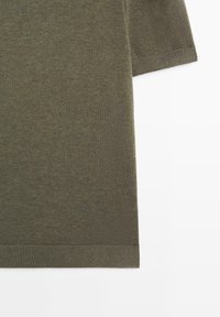 Sezione di camicia a maniche corte in tessuto di maglia verde oliva con polsini e orlo a coste su sfondo bianco.