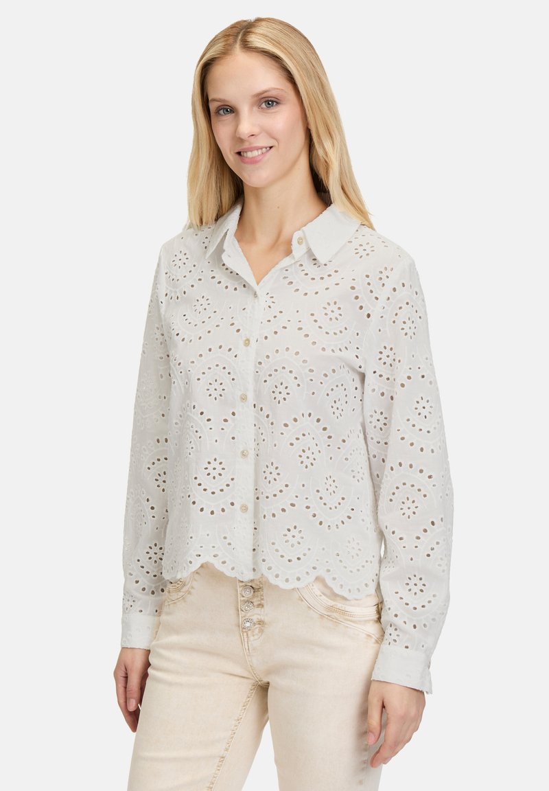Weiße Baumwollbluse mit knopffixiertem Kragen, Lochmuster und gewelltem Saum; lange Ärmel, leicht und halbtransparent.
