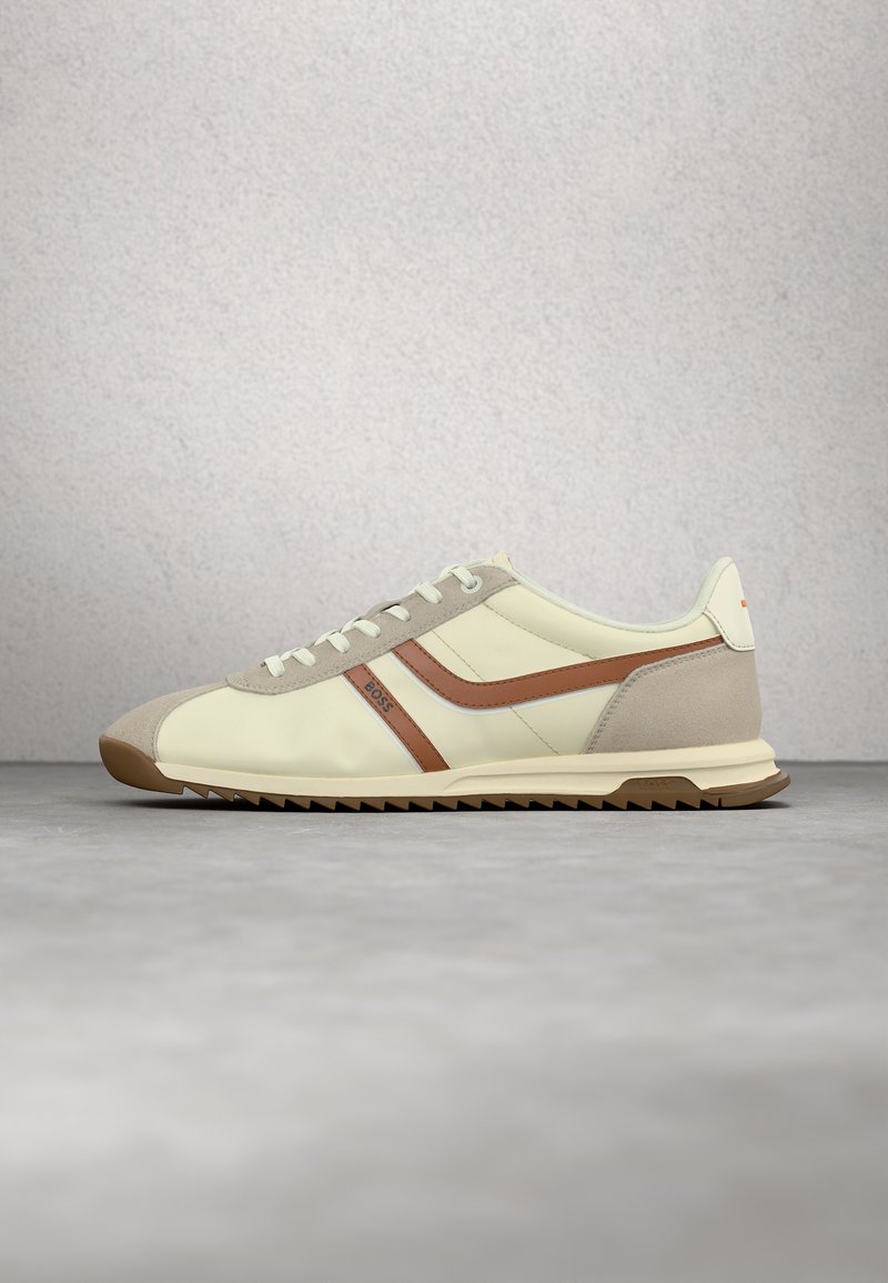 Baskets beige et marron à lacets avec semelle en caoutchouc et logo BOSS sur le côté, présentées sur une surface grise avec un fond neutre.