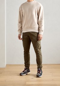 Beżowy sweter, oliwkowe spodnie cargo i wielokolorowe sneakersy. Sweter ma okrągły dekolt; spodnie mają kieszenie cargo; sneakersy mają amortyzowaną podeszwę.