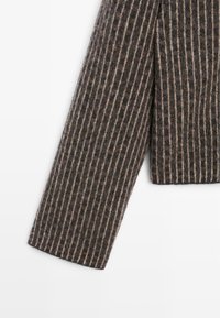 Rękaw wełnianej kurtki w ciemnym brązie z pionowymi beżowymi paskami, o teksturowanej powierzchni i prostym kroju. Brak widocznych elementów metalowych lub akcentów.