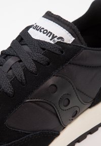Scarpa sportiva nera realizzata in materiali suede, nylon e pelle. Profilo basso con lacci rotondi, colletto imbottito e logo sulla linguetta.