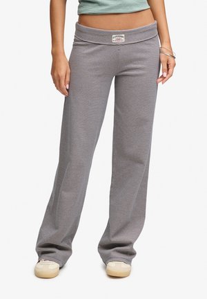 Femme portant un pantalon large rayé noir et blanc avec une étiquette à la taille, associé à des chaussures blanches décontractées et un crop top bleu clair.