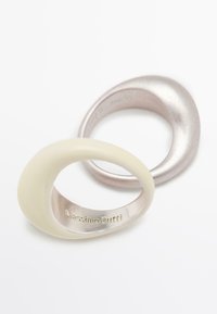 Due anelli: uno crema opaco e uno argento metallico, entrambi con forme lisce e organiche. "Massimo Dutti" è inciso sul lato interno dell'anello crema.