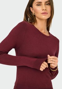 Bordeaux gebreide trui met lange mouwen, geribbelde manchetten en een ronde hals. Zachte textuur met een aansluitende pasvorm, met minimale details.