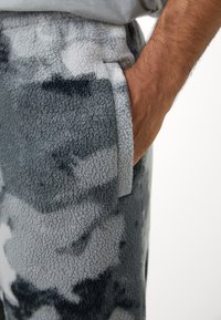 Szürke árnyalatú polárnadrág, puha tapintással és absztrakt mintázattal. Kényelmet biztosító oldalsó zsebből áll.