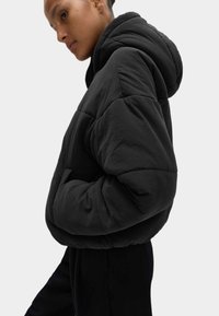 Giubbotto a vento nero con cappuccio, realizzato in tessuto texturizzato e con una silhouette rilassata. Include tasche laterali e dettagli di cucitura visibili.