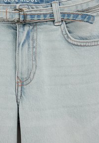 Helesinised teksad kergelt tuhmendatud viimistlusega, millel on vööaasad, oranž õmblusdetail ja taskud mõlemal küljel.