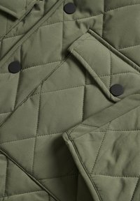 Gepolsterter Mantel oder Jacke aus olivgrünem, gestepptem Stoff mit diagonaler Naht und schwarzen Druckknöpfen.