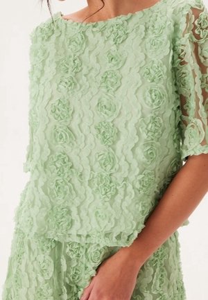 Haut vert menthe avec un motif floral texturé et des applications de roses en relief. Manches courtes et encolure bateau complètent le design.