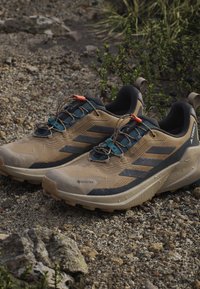 Beżowe wodoodporne buty trekkingowe z ciemnymi akcentami, teksturowana siateczka górna, wyściełany kołnierz oraz podniesiona gumowa podeszwa dla lepszej przyczepności.