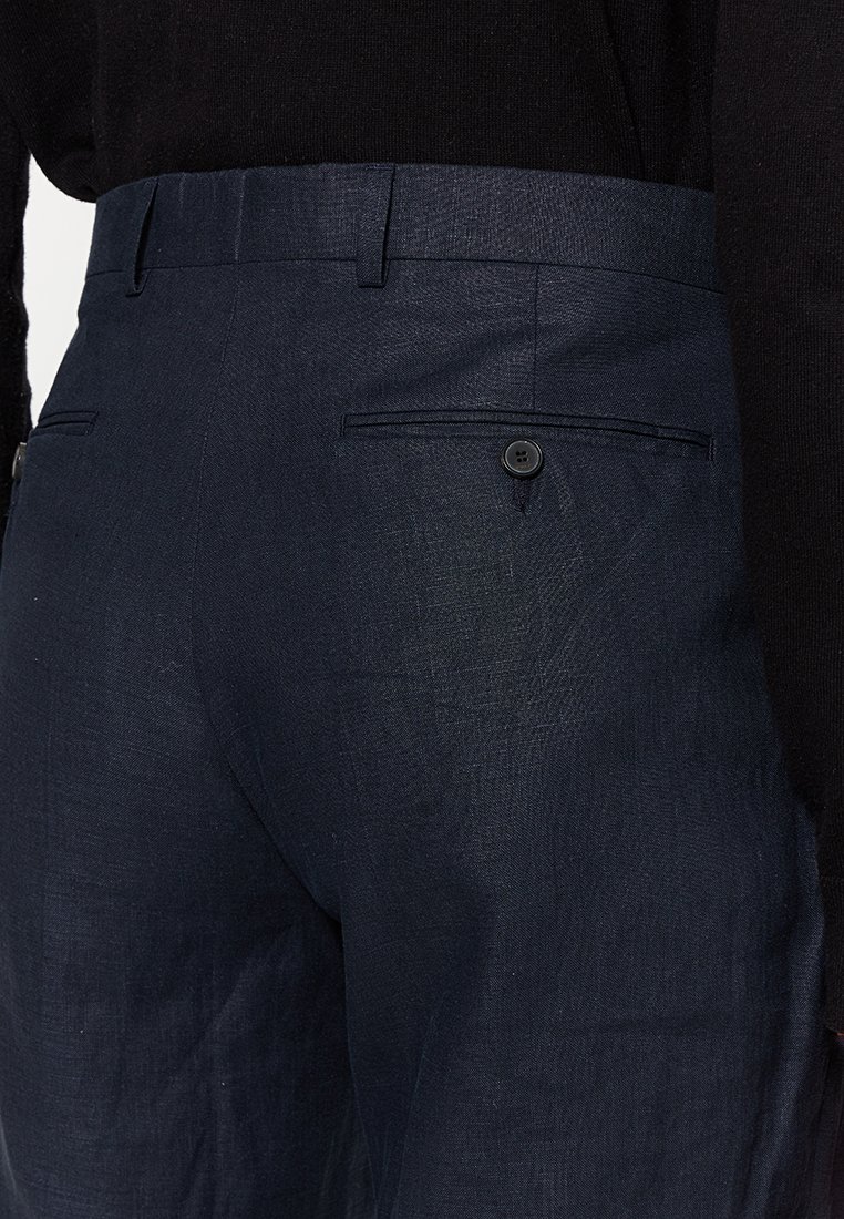 Nahaufnahme von dunkelblauen, maßgeschneiderten Hosen mit geknöpftem Gesäßtasche und Gürtelschlaufen, kombiniert mit einem schwarzen Oberteil.
