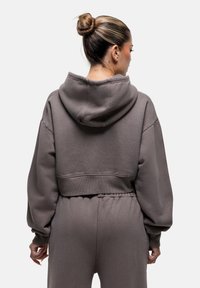 Felpa con cappuccio corta di colore grigio scuro, realizzata in materiale morbido, con una vestibilità rilassata e orlo a coste, abbinata a pantaloni jogger coordinati.