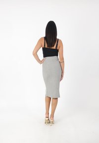 Grijze knielange rok met een getailleerd ontwerp, zachte textuur en subtiele stretch. Zwarte tanktop met dunne bandjes. Beige hoge hakken.