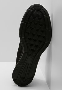 Semelle de chaussure de sport noire avec un motif de grip texturé en forme d'hexagone et des bords lisses. Fabriquée en caoutchouc, elle présente des reliefs latéraux pour la stabilité.