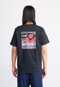 Zwart t-shirt met korte mouwen, voorzien van een kleurrafische afbeelding van bergen en een zon op de achterkant, met de tekst "COLUMBIA" erboven.