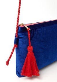 Clutch in velluto blu con una tracolla rossa attorcigliata e dettaglio a frangia. Presenta una cerniera dorata e una fodera rosa. Forma rettangolare compatta.