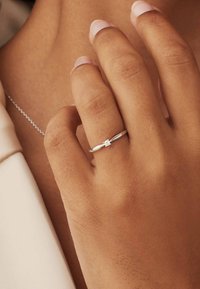 Silberring mit einem glatten Band und einem zentralen klaren Edelstein. Sanft auf der Haut platziert, zeigt er den natürlichen Nagel-Finish und die Textur.