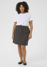 Jupe grise, longueur genoux, en tissu léger, avec une taille élastique et un détail de lien à l'avant, associée à un T-shirt blanc et des ballerines noires.