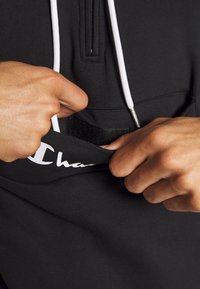 Felpa nera con cappuccio e lacci bianchi, dotata di collo zip e tasca con patta in velcro; logo stampato in bianco all'orlo.