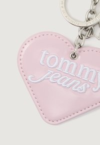Rózsaszín, szív alakú kulcstartó fehér "tommy jeans" hímzéssel és csatlakoztatott ezüst színű fém lánccal és gyűrűvel.