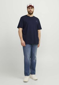 Navy cotton t-shirt with short sleeves, relaxed fit, paired with light blue denim jeans and white sneakers, worn with a baseball cap.