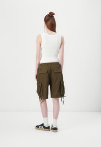 Grønne cargo-shorts med lommer og snøring, kombinert med en tettsittende hvit tanktop og svarte joggesko.
