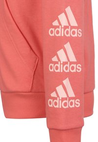 Sudadera coral con puños acanalados, bolsillo canguro y tres logotipos blancos de Adidas a lo largo de la manga. Tejido suave y texturizado.